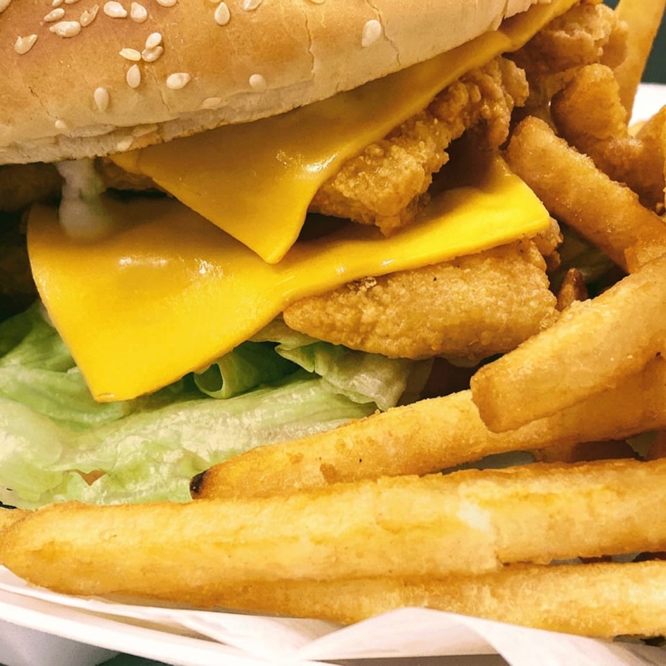 Close-up of a sesame-seed chicken sandwich with melted cheese, lettuce, and fried chicken, served with golden fries.