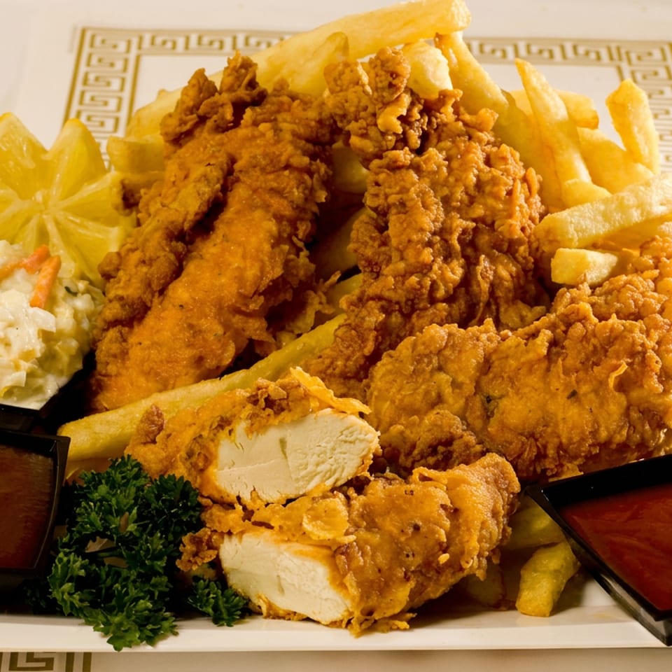 Golden fried chicken tenders and fries served with lemon, coleslaw, parsley, and two dipping sauces on a decorative platter.