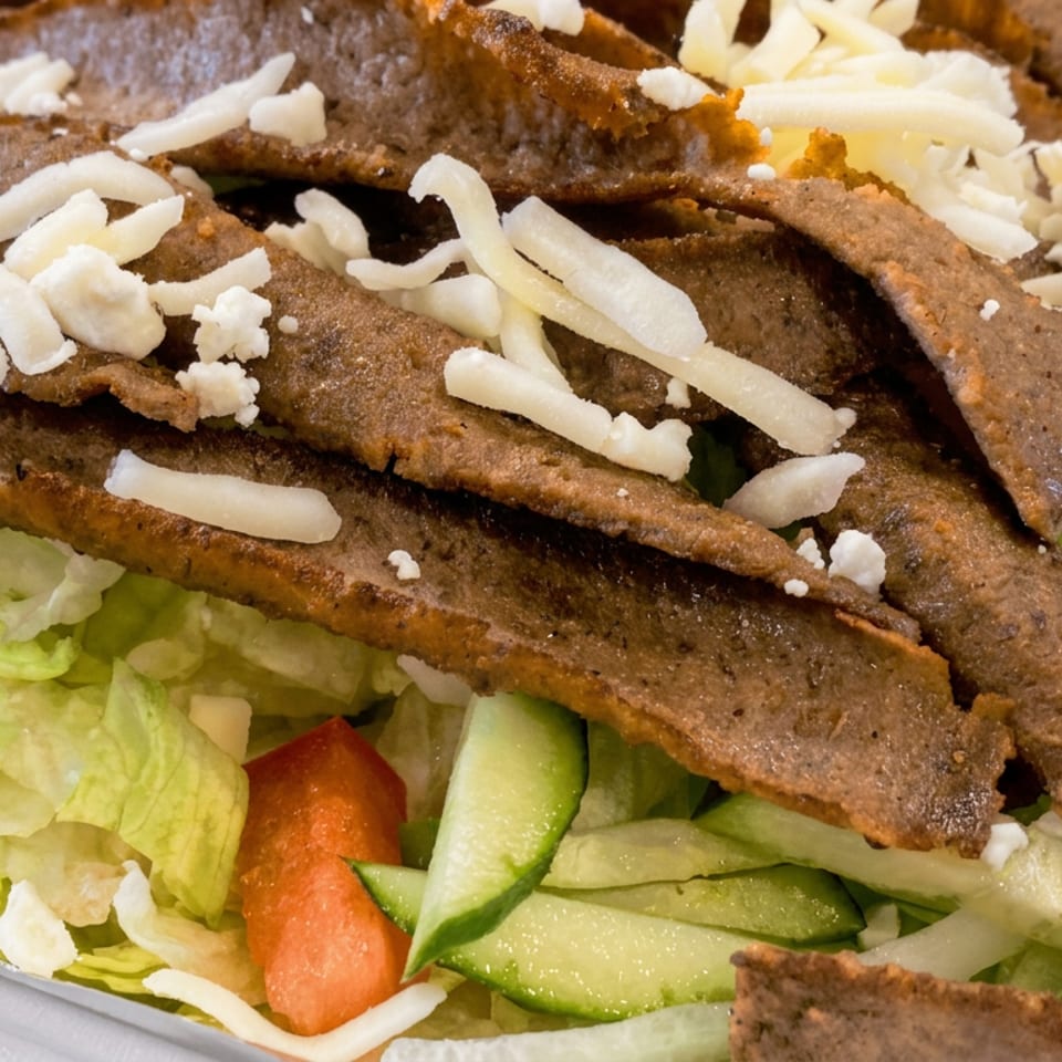 Greek salad topped with seasoned grilled beef strips, shredded cheese, feta, lettuce, tomatoes, and cucumber.
